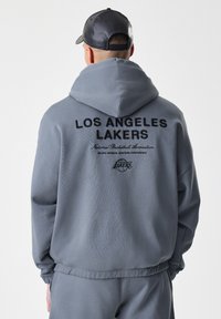 Felpa grigia con cappuccio caratterizzata dalla scritta "LOS ANGELES LAKERS" in testo nero sul retro, con ulteriori logo e una vestibilità comoda.