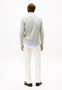 Suéter gris claro, mangas largas, escote en V; sobre una camisa a rayas azules. Pantalones blancos y zapatos negros con suela gruesa. Estilo minimalista.