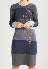 Långärmad klänning med horisontella grå och marinblå ränder. Utrustad med blommig broderi i brunt och vitt på framsidan. Mjukt material, figurnära passform.