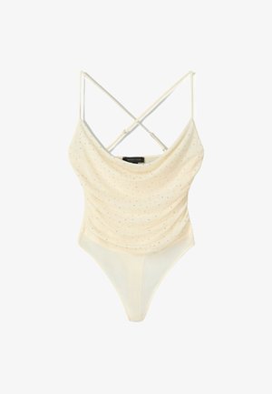 Cream bodysuit with cowl neckline, cross-back straps, and sparkling silver dots. Smooth fabric with a high-cut leg design.