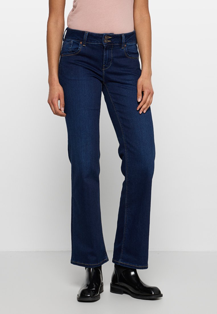 Dunkelblaue, gerade geschnittene Jeans mit Knopfverschluss, Gürtelschlaufen und dezentem Stitching. Das Tragen von schwarzen Knöchelboots vervollständigt den Look.