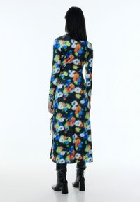 Langärmliges, eng anliegendes Kleid aus leichtem Stoff mit einem mehrfarbigen Blumenmuster auf schwarzem Hintergrund, tailliert mit einem Gürtel.