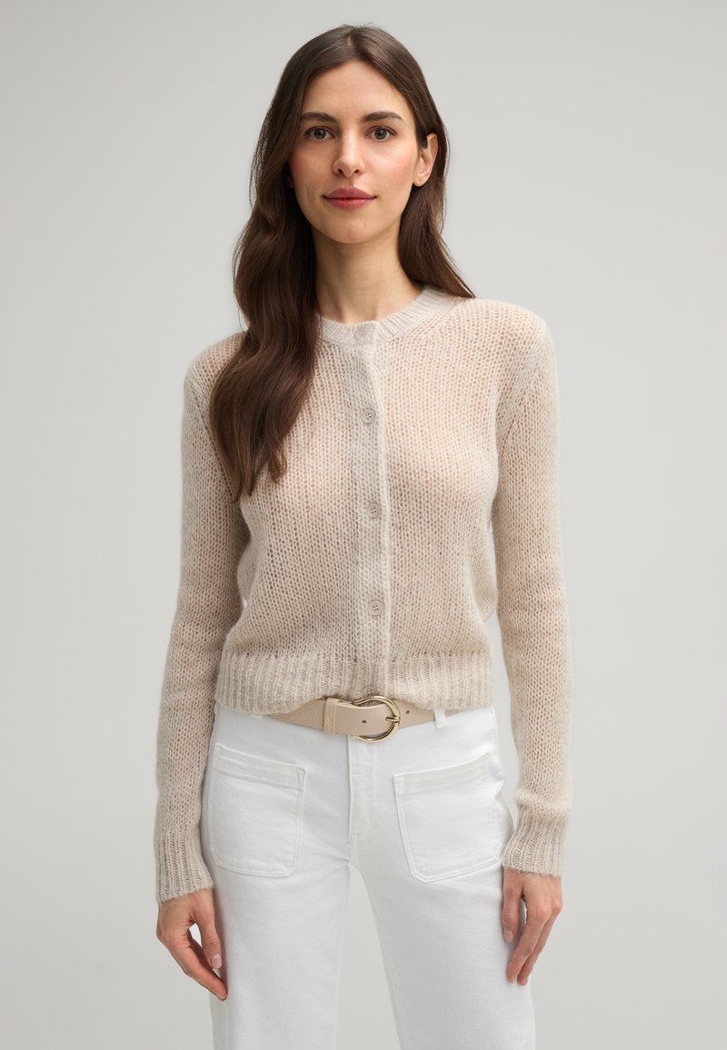 Helle beige, gestrickte cardigan mit Knopfleiste, runder Halslinie, langen Ärmeln und gerippten Bündchen. Kombiniert mit weißen Hosen und einem beigen Gürtel.