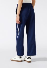 Marineblauwe joggingsbroek met witte zijkanten, elastische tailleband en zijzakken. Gecombineerd met witte sneakers met een zwart logo-accent.