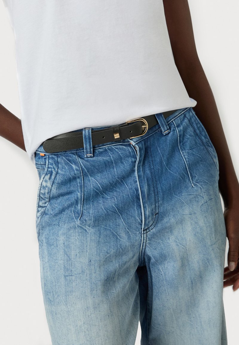 Jean en denim bleu clair à texture délavée, avec une ceinture noire à boucle dorée. Associé à un t-shirt blanc uni.