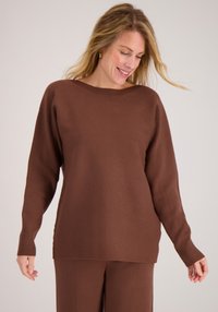 Bruine gebreide trui met een brede halslijn, lange mouwen en geribbelde manchetten. Zachte textuur, relaxte pasvorm, gecombineerd met bijpassende bruine broek.