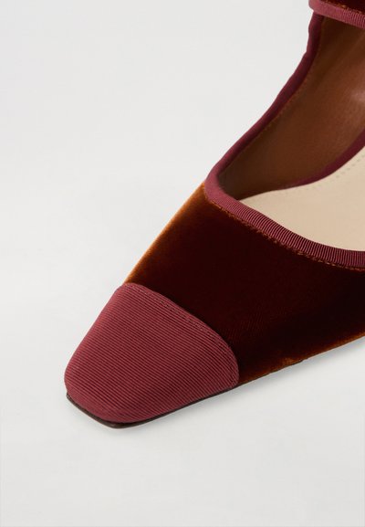 Röd sammetspumps med spetsig tå och en ruggad vinröd spets, kompletterad med en slät innersula och ett smalt rem.