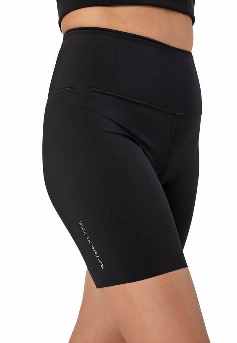 Κοντινό πλάνο ενός ατόμου που φοράει μαύρο ψηλόμεσο σορτς συμπίεσης με μικρό λευκό κείμενο στο πλάι που γράφει «Η διαδρομή σου. Χωρίς ίχνη.»