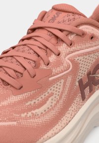 Une paire de chaussures de sport corail avec un dessus en maille texturée, des lacets plats et une semelle lisse et rembourrée avec un détail de logo contrastant.