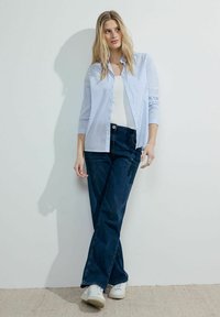 Light blue striped button-up shirt over a white tank top, paired with dark blue jeans and white sneakers. Smooth textures, casual fit.