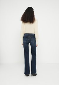 Tmavomodré džínsy s rozšírenými nohavicami, stredne vysokým pásom, jemným prešívaním a zadnými vreckami. Kombinované s svetlým krémovým svetrom.