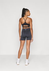 Sostegno sportivo nero con dettaglio tagliato sulla schiena, abbinato a pantaloni corti neri coordinati. Entrambi realizzati in materiale morbido ed elastico.