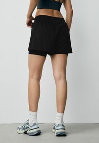 Černé sportovní šortky s elastickým páskem, spárované se světle modrými běžeckými botami a bílými kotníkovými ponožkami. Minimalistický design, hladká textura.