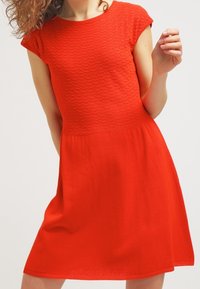 Röd klänning med en texturerad överdel och korta ärmar, som vidgar sig från midjan. Slät tyg med rund halsringning och knäl ång fåll.