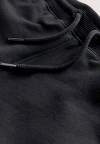 Zwarte sweatpants met een zachte textuur, voorzien van een trekkoord met schuifknop, geribde tailleband en een gladde stofafwerking.