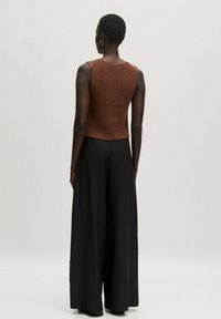 Brauner, gestrickter ärmelloser Top mit strukturiertem Muster, kombiniert mit schwarzen weit geschnittenen Hosen und Ankle Boots, von hinten betrachtet.