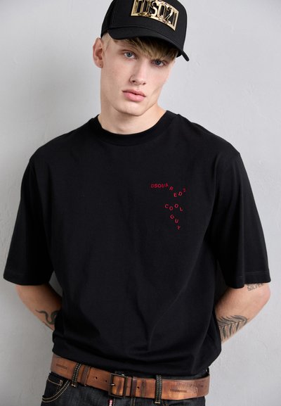 Must t-särk lühikeste varrukatega, millel on punane trükitud tekst "DSQUARED COOL GUY". Seljas pruun vöö ja must kapuuts, millel on kuldne logo.