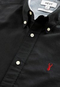 Camisa negra ajustada de algodón con botones blancos y un logotipo de langosta rojo bordado en el pecho.