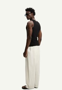 Black sleeveless tank top paired with loose white striped pants and black sandals, featuring a relaxed fit and no visible patterns.