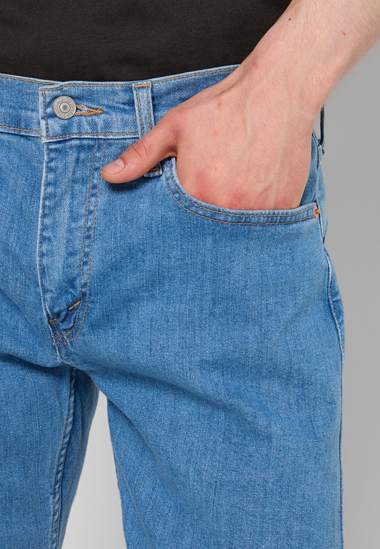 Jean en denim bleu clair avec un design à cinq poches. Comprend une fermeture à bouton métallique, des coutures visibles et une coupe décontractée.