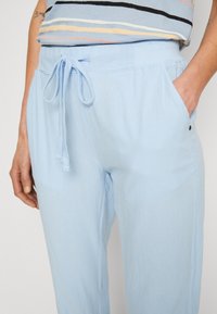 Lichtblauwe, zachte stoffen broek met een elastische tailleband, trekkoord, zijzakken en een relaxte pasvorm. Soepele textuur met minimale details.