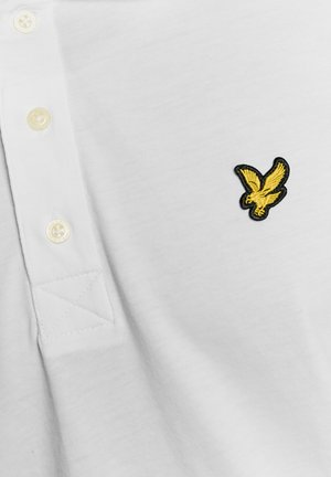 Bílá polokošile se třemi krémovými knoflíky a malým žlutým vyšívaným logem ptáčka na hrudi.