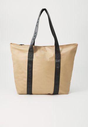 Tan tote bag med en glat stofoverflade, sorte logo-præget stropper og en lynlåslukning i toppen. Firkantet form med bløde kanter.