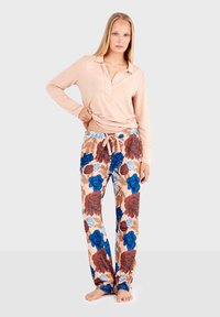 Haut à manches longues rose clair avec un col boutonné, associé à un pantalon à motifs floraux dans des tons rouge, bleu et beige. Ceinture élastique avec cordon de serrage.