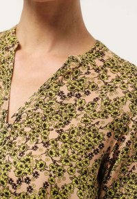 Blouse fleurie avec une base rose clair ornée de motifs floraux jaunes et noirs, un décolleté en V, et un tissu doux et léger.