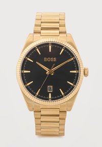 Χρυσό μεταλλικό ρολόι χειρός με μαύρο καντράν, χρυσά σημάδια ωρών, λογότυπο "BOSS" και παράθυρο ημερομηνίας στη θέση 6, που δείχνει ώρα 10:10:35.