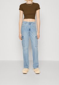 Camiseta corta marrón, jeans cargo azules con bolsillos laterales y calzado beige de felpa. Diseño simple, tejido suave, ajuste casual.