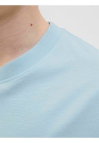 Světle modré tričko s kulatým výstřihem vyrobené z hladké bavlněné tkaniny. Obsahuje žebrovaný límec a bezšvový design ramene.