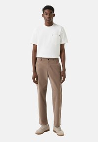 Hvid kortærmet t-shirt med lomme, kombineret med brune fløjlsbukser og lyse sneakers. Enkel design og afslappet pasform.