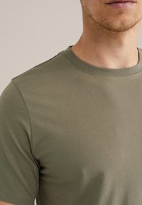 Camiseta de algodón verde oliva con escote redondo y mangas cortas, con una textura suave y sin patrones ni acentos visibles.