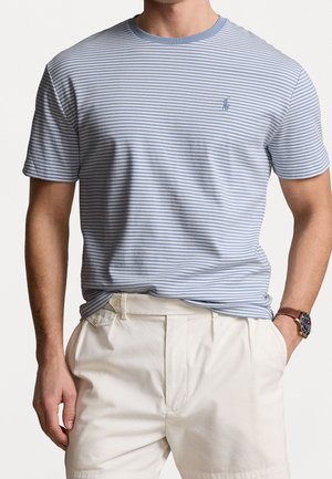 T-shirt à manches courtes rayé bleu clair et blanc, en coton, col rond, petit logo sur le côté gauche de la poitrine, associé à un short de couleur crème.