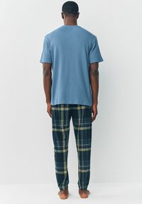Blaues, kurzärmeliges, strukturiertes T-Shirt kombiniert mit karierten Flanellhosen in Dunkelgrün, Marineblau und Gelb, mit elastischen Bündchen an den Knöcheln.