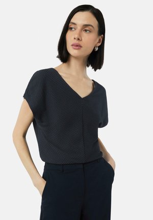 Navy short-sleeve top with a V-neck, featuring a textured fabric and subtle stripe pattern, paired with high-waisted dark pants.
