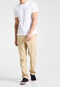 Vit bomullströja med rund halsringning, beiga raka chinos och mörkblå skor med vit sula. Enkla och avslappnade kläder.