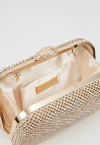 Borsa clutch realizzata in metallo dorato scintillante con chiusura gioiello. L'interno presenta una fodera in satin e una piccola tasca.