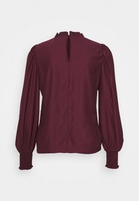 Blouse prune à manches longues avec poignets froncés, épaules bouffantes et col montant avec une ouverture en forme de goutte à l'arrière.