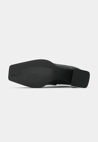 Semelle de chaussure à talons hauts noire avec une forme plate et large. Présente un caoutchouc texturé pour l'adhérence et une zone de talon lisse, légèrement surélevée.