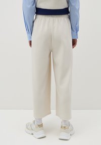 Pantaloni sportivi larghi color crema con vita elastica, abbinati a calze bianche e scarpe da ginnastica beige con dettagli metallici.