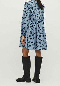 Sininen mekko mustilla leopardikuvioilla, röyhelöhartioilla, vyötäröstä kootulla ja pitkillä hihoilla. Yhdistetty polven yli ulottuviin mustiin saappaisiin.