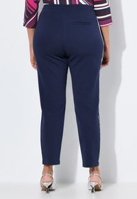 Marineblauwe broek van rekbaar materiaal, met een slim fit, zijstrepen en een achterzak, gecombineerd met zilveren hoge hakken.