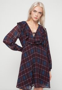 Πλαΐν φόρεμα σε αποχρώσεις μπορντό και μπλε, με βαθύ V-ντεκολτέ, ρυάκι στον λαιμό και μακριά μανίκια με ρευστή σιλουέτα.