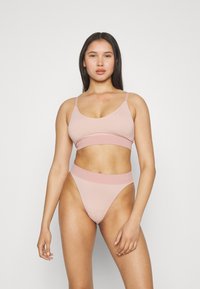 Lichtroze bralette met een geribbeld band en dunne bandjes, gecombineerd met een bijpassende hoge taille thong. Gladde textuur, minimalistisch ontwerp.