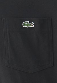 Black pocket t-shirt featuring a green and red embroidered crocodile logo on the left chest pocket. Fabric appears smooth and slightly textured.