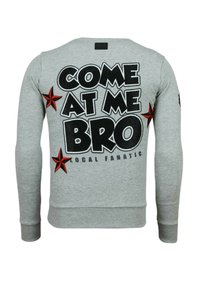 Grijze sweatshirt met grote zwarte tekst "COME AT ME BRO" op de achterkant, rode steraccenten en geribbelde boorden en zoom.
