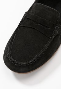 Black suede loafers with a stitched outline, featuring a smooth texture and a small decorative strap across the front.