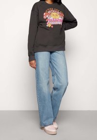 Tmavě šedá mikina s barevným grafickým motivem; široké světlé modré džíny; růžové tenisky; volný střih; měkká textilie.